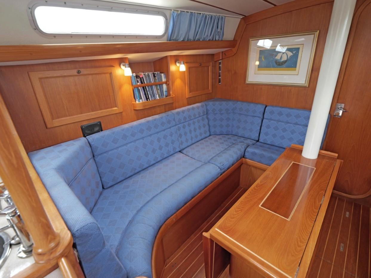 Cozy interior of 1999 Rustler 42 yacht with blue seating and wooden finish.