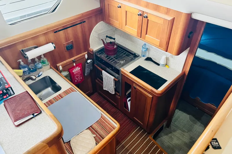 Tranquil Tides Yacht Photos Pics 2006 Mainship 34 Trawler kitchen with wooden cabinetry, stove, and sink. Cozy and functional design.