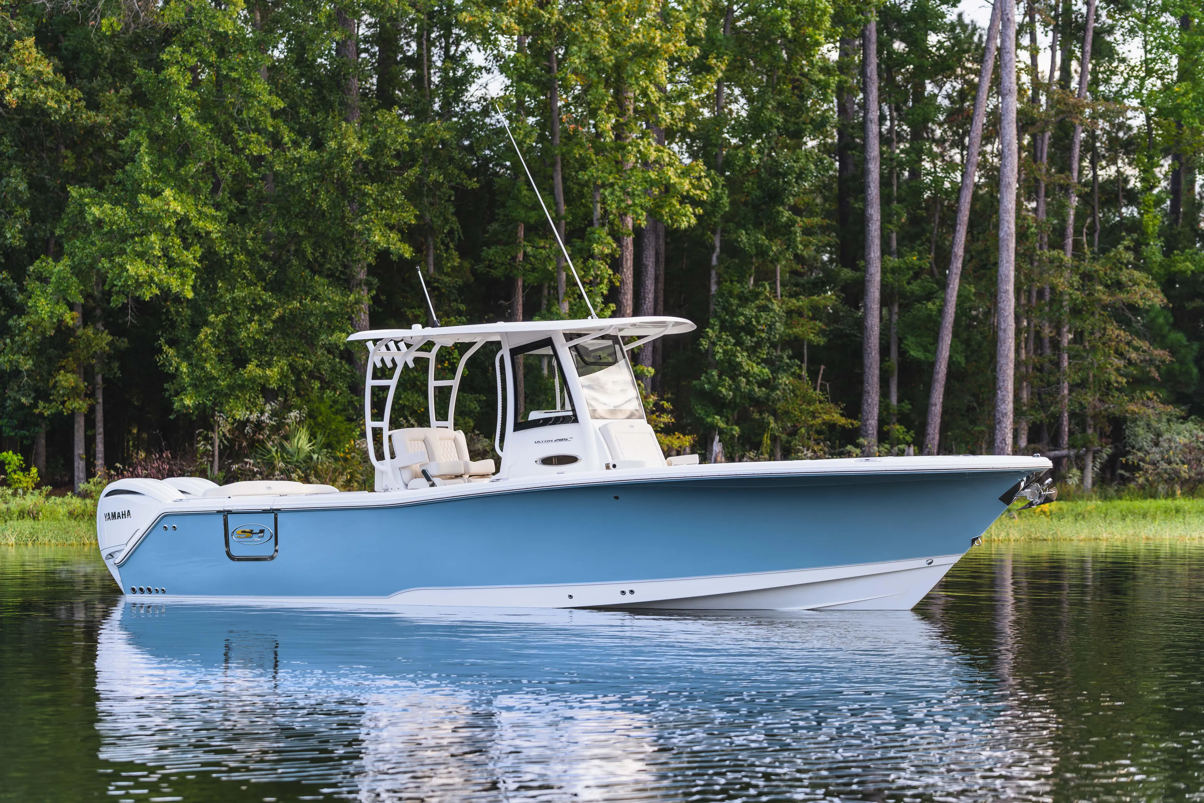  Yacht Photos Pics 2026 Sea Hunt Ultra 285 Coffin Box boat on calm water, surrounded by lush trees.
