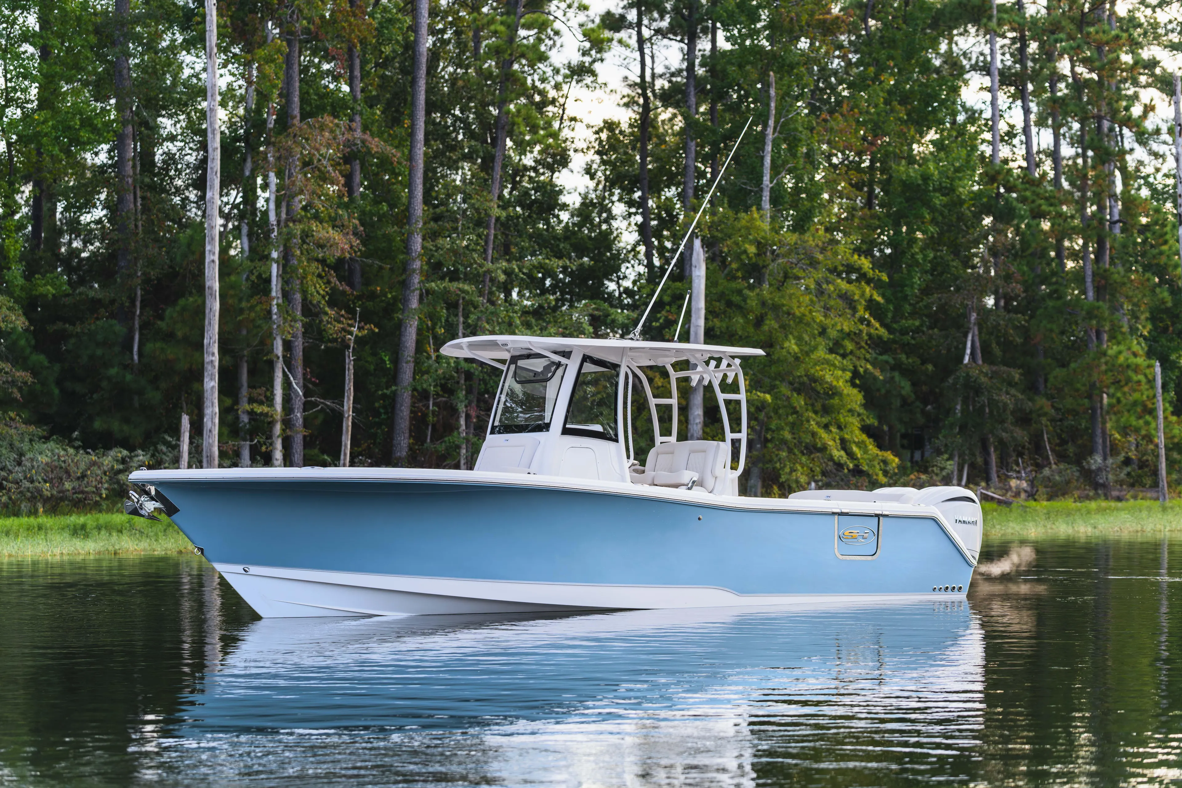  Yacht Photos Pics 2026 Sea Hunt Ultra 285 Coffin Box boat on calm water, surrounded by lush trees.