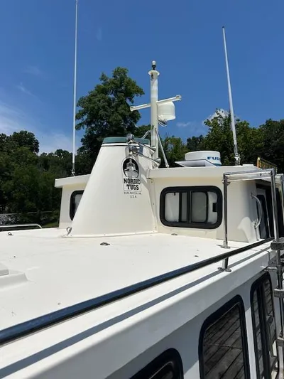 Forget Me Knot Yacht Photos Pics 2001 Nordic Tug 32 boat with white exterior, docked near trees under a clear blue sky.