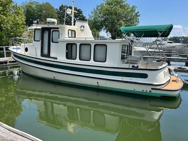 Forget Me Knot Yacht Photos Pics 2001 Nordic Tug 32 boat docked on calm water with green canopy and scenic background.