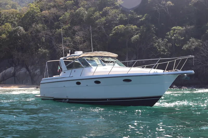 La Ultima Chica Yacht Photos Pics 1997 Tiara Yachts Express boat cruising on clear water near a forested shoreline.