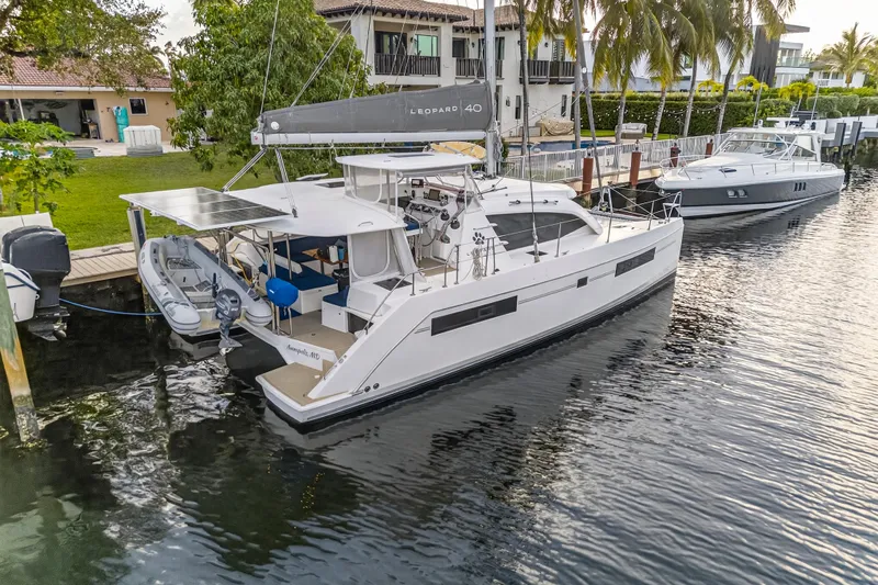 Changing Keys Yacht Photos Pics 2020 Leopard 40 catamaran docked by waterfront homes, featuring solar panels and a dinghy.