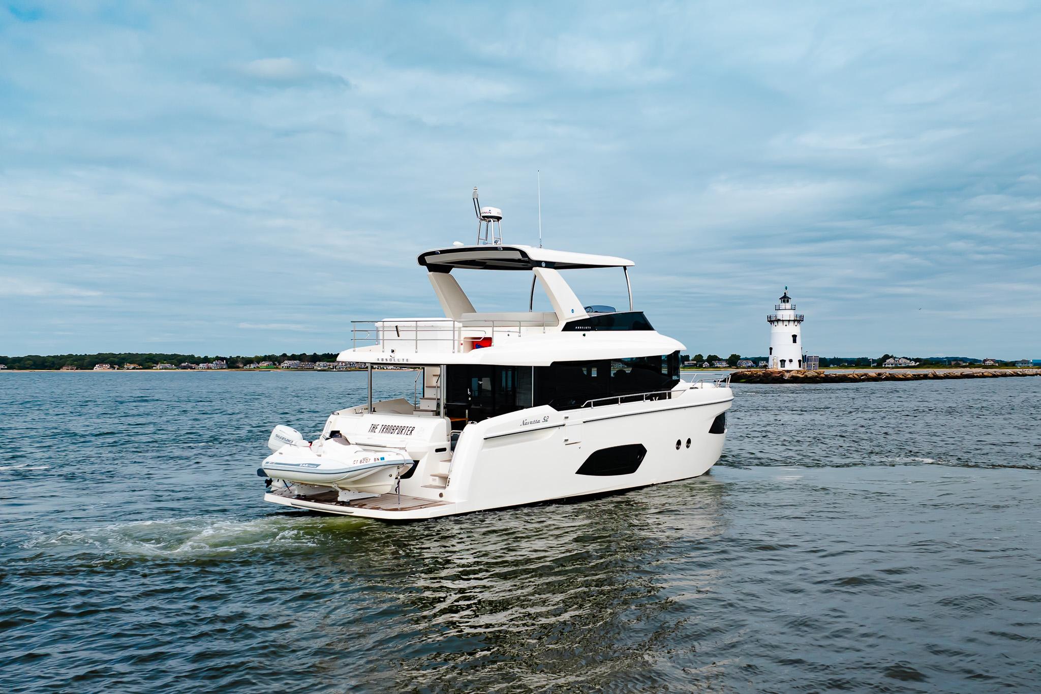 2023 Absolute 52 Navetta yacht cruising near a lighthouse on a calm sea.