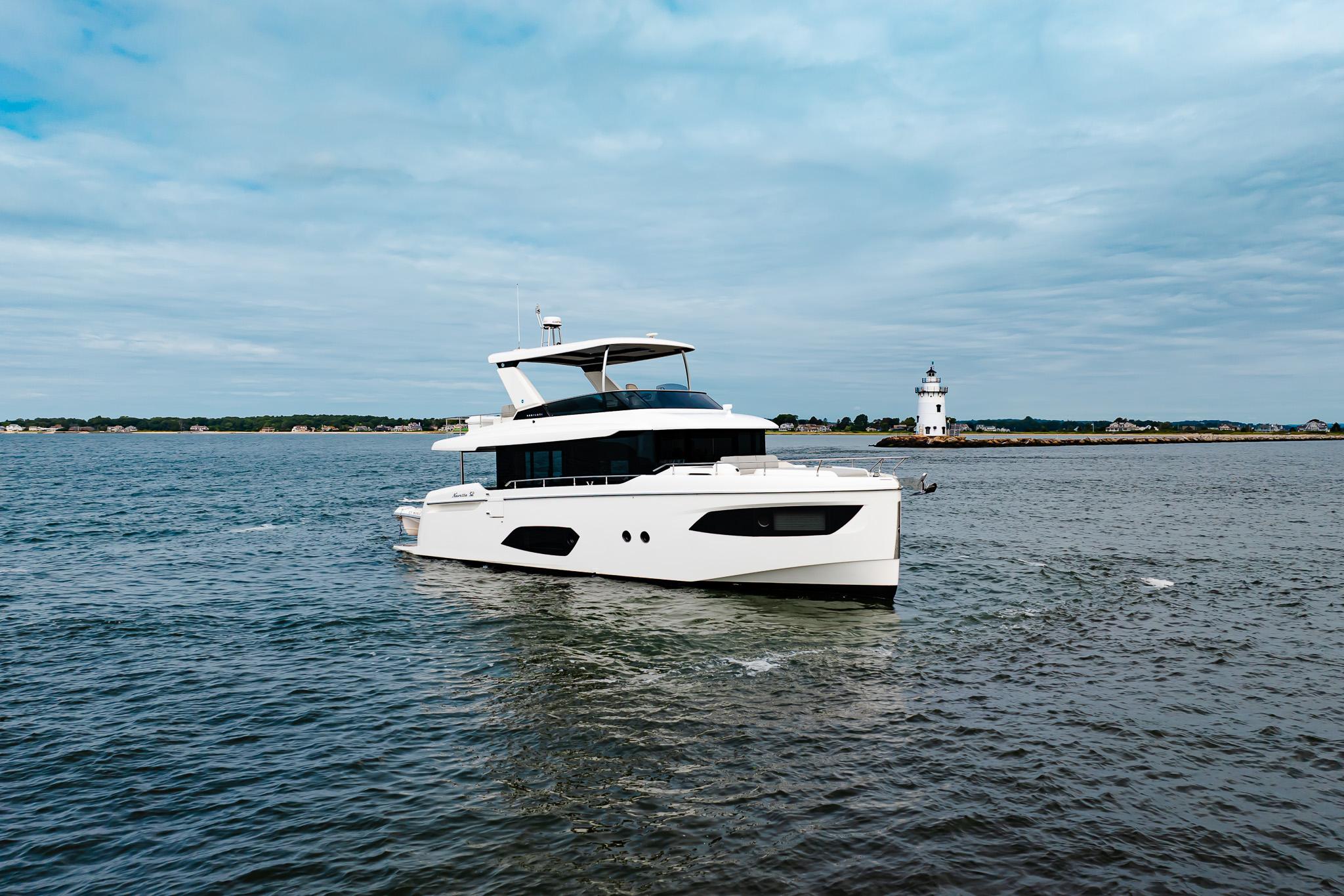 2023 Absolute 52 Navetta yacht cruising near a lighthouse on a cloudy day.