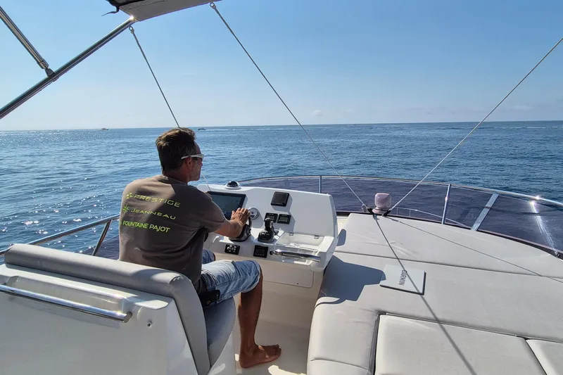 Ker Lann Yacht Photos Pics Man steering a 2022 Prestige 460 yacht on open sea under clear skies.
