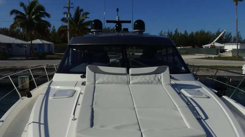 Chapter II Yacht Photos Pics 2023 Riviera 6000 Sport Yacht with sunbed, docked near palm trees and clear skies.