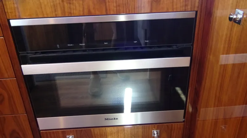 Chapter II Yacht Photos Pics Modern Miele oven in 2023 Riviera 6000 Sport Yacht kitchen, featuring sleek wood paneling.
