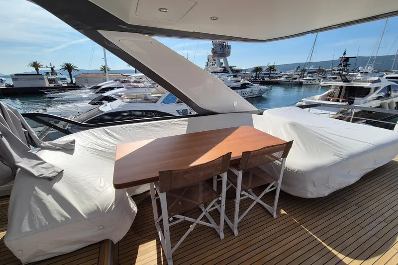  Yacht Photos Pics Luxurious 2023 Azimut Fly 68 yacht deck with covered seating and wooden table, docked at marina.