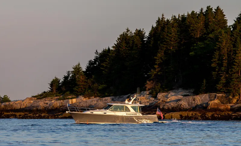 Call For Availability Yacht Photos Pics 2025 Sabre 43 Salon Express yacht cruising near a forested rocky shoreline.