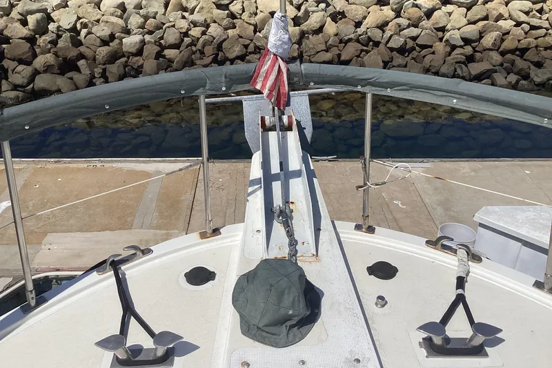 No Reservations Yacht Photos Pics 1984 Spindrift 52 Motor Yacht bow with flag, docked near rocky shoreline.