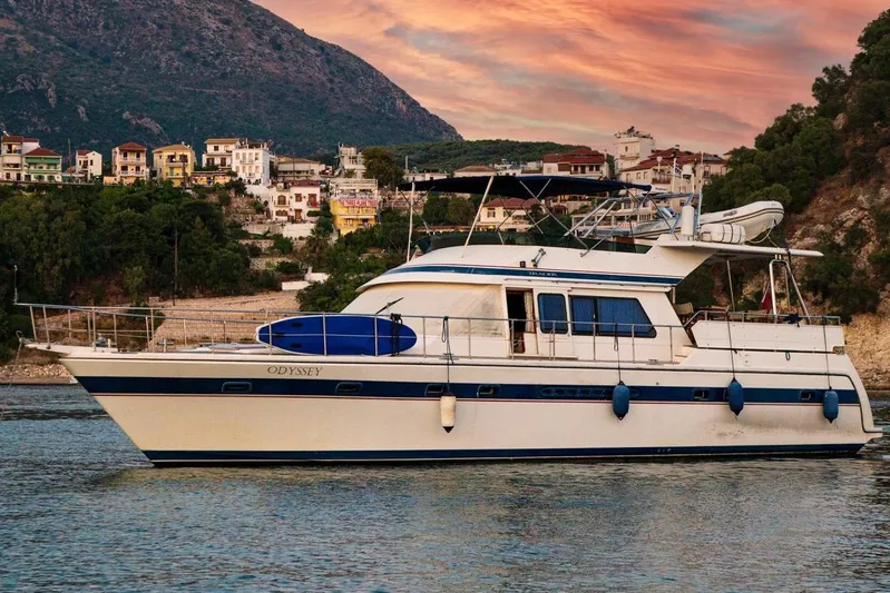 Odyssey Yacht Photos Pics Trader Sunliner 625 yacht from 2000, docked near a scenic coastal village at sunset.