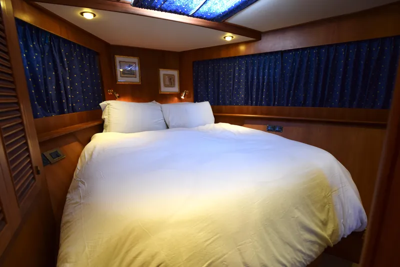Odyssey Yacht Photos Pics Cozy bedroom in 2000 Trader Sunliner 625 yacht with wood paneling and blue curtains.