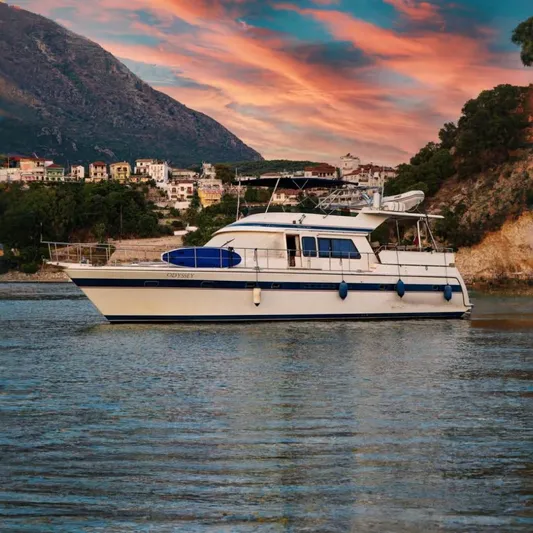 Odyssey Yacht Photos Pics Trader Sunliner 625 yacht from 2000, docked near a scenic coastal village at sunset.