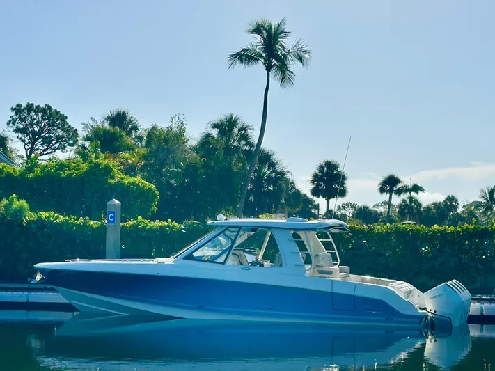Hightide Yacht Photos Pics 2022 Boston Whaler 380 Realm boat docked near palm trees, reflecting on calm water.