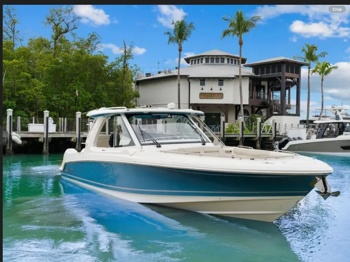 Hightide Yacht Photos Pics 2022 Boston Whaler 380 Realm boat docked near waterfront building, surrounded by palm trees.