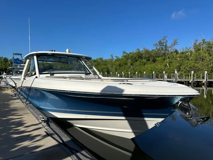 Hightide Yacht Photos Pics 2022 Boston Whaler 380 Realm docked, reflecting on calm water under clear blue sky.