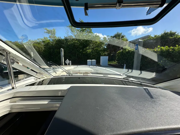 Hightide Yacht Photos Pics 2022 Boston Whaler 380 Realm cockpit view with open windshield, surrounded by greenery.
