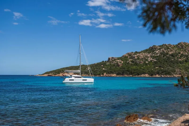  Yacht Photos Pics Sailboat Lagoon 38 (2026) anchored in clear blue waters near a rocky coastline.