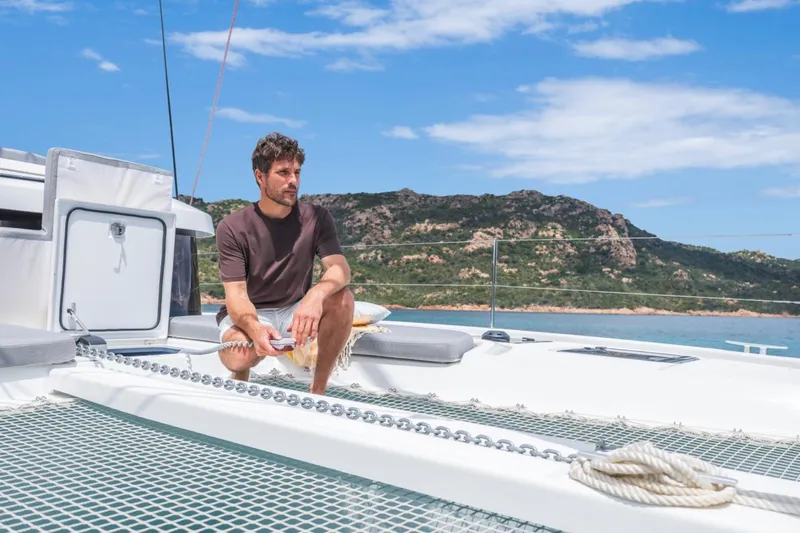  Yacht Photos Pics Man relaxing on Lagoon 38 catamaran, 2026 model, with scenic coastal backdrop.
