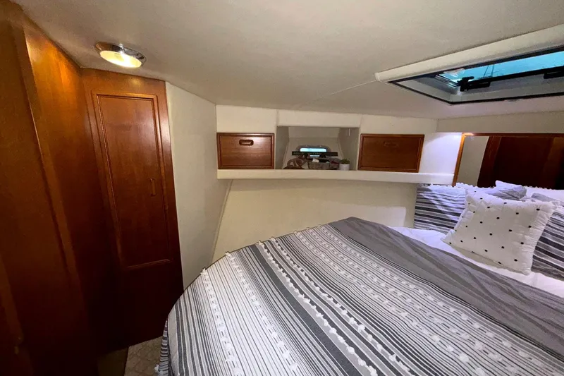  Yacht Photos Pics Cozy bedroom in 1996 Riviera 39 Open Flybridge yacht with striped bedding and wooden cabinets.