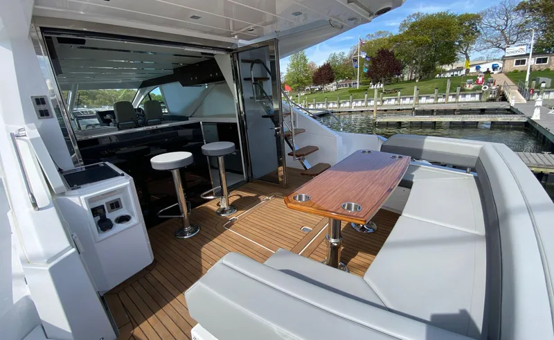 Radiant Yacht Photos Pics 2022 Cruisers Yachts 60 Fly deck with seating, table, and bar stools, docked by the water.