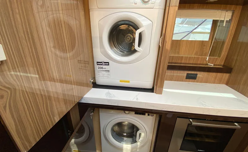 Radiant Yacht Photos Pics Laundry area in 2022 Cruisers Yachts 60 Fly, featuring modern appliances and wood cabinetry.