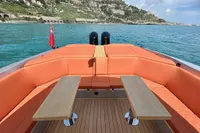 2023 SACS Strider 15 FB boat with orange seating and wooden tables on a scenic coastline.