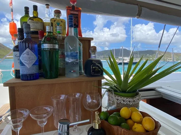 The Recipe Yacht Photos Pics Bar setup on Lagoon 560 yacht with liquor bottles, glasses, and fruit, against a scenic ocean backdrop.
