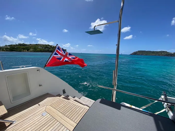 The Recipe Yacht Photos Pics Lagoon 560 yacht deck with British flag, overlooking turquoise sea and clear blue sky.
