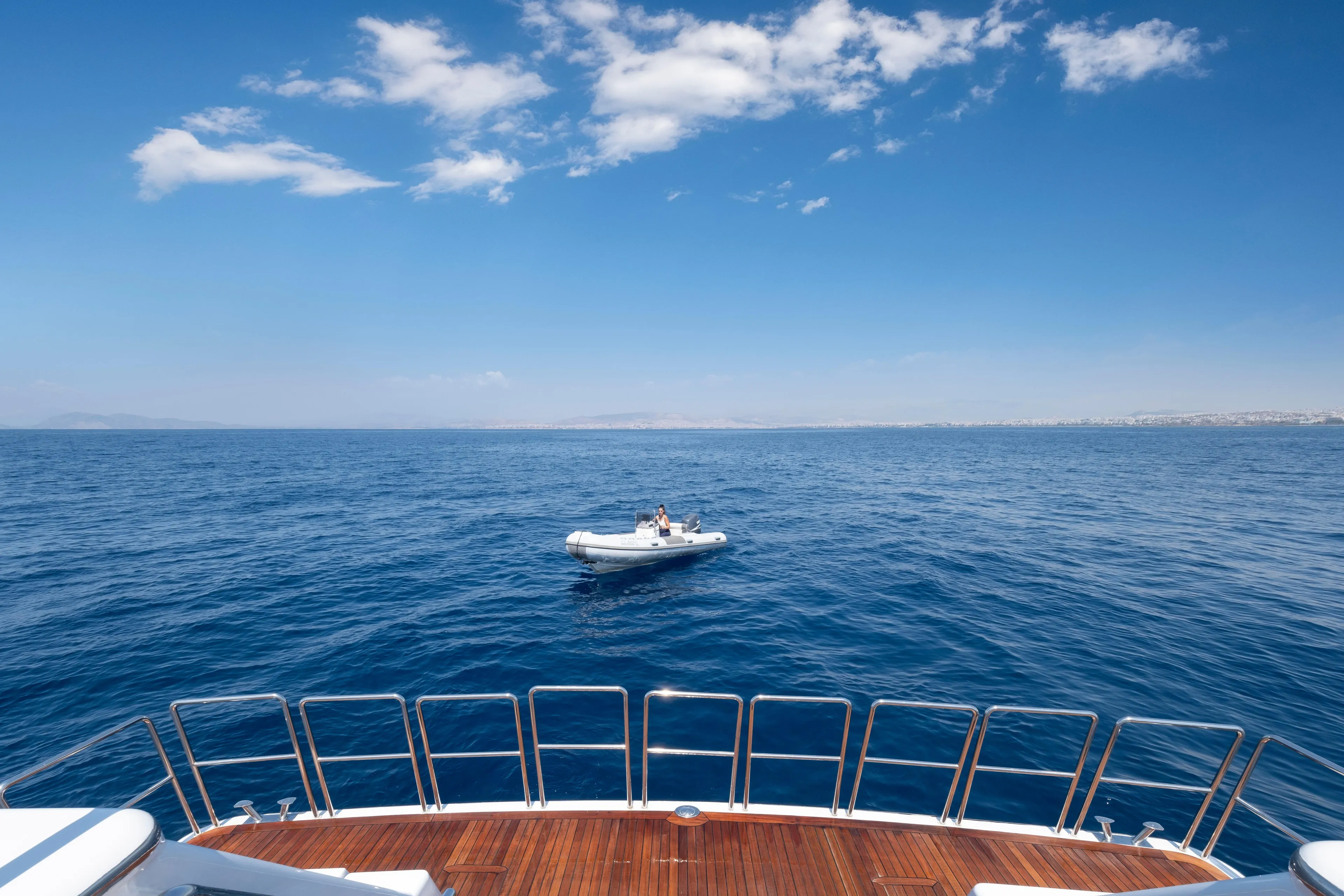 Yacht deck view with small boat on open sea, clear blue sky.