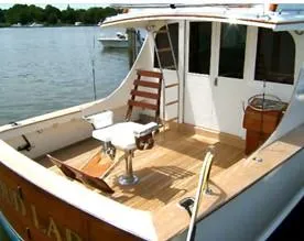 Proud Lady Yacht Photos Pics 1957 Rybovich Convertible boat with wooden deck and fishing chair on a calm lake.