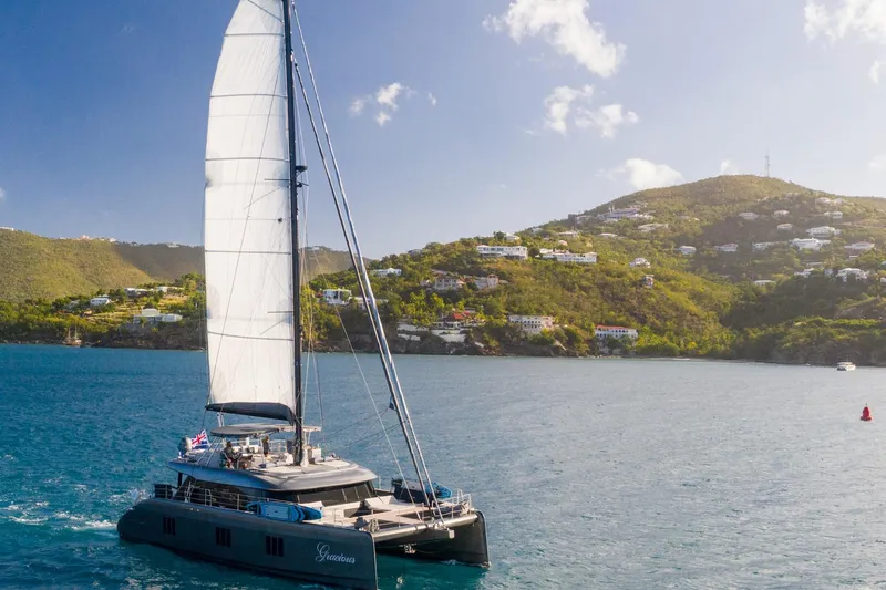 Gracious Yacht Photos Pics 2021 Sunreef 60 sailing catamaran cruising near scenic coastal hills.