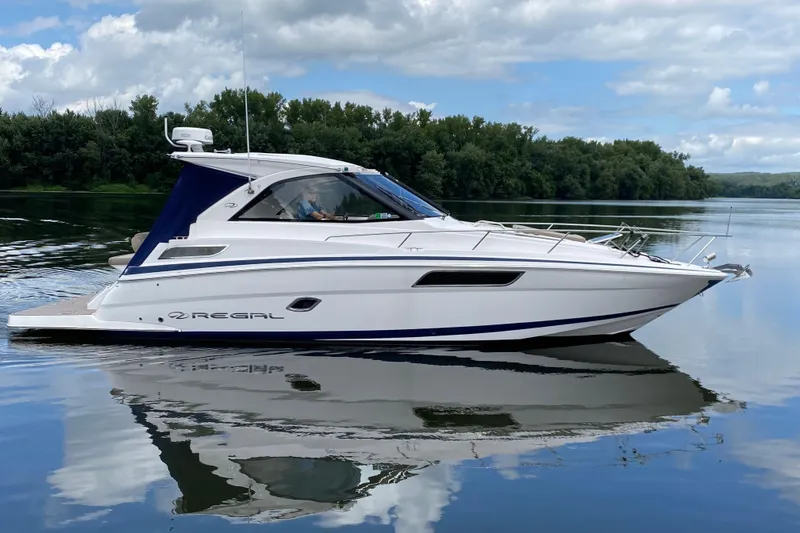 Just Traded Yacht Photos Pics 2014 Regal 35 Sport Coupe on calm water, surrounded by lush greenery and cloudy sky.