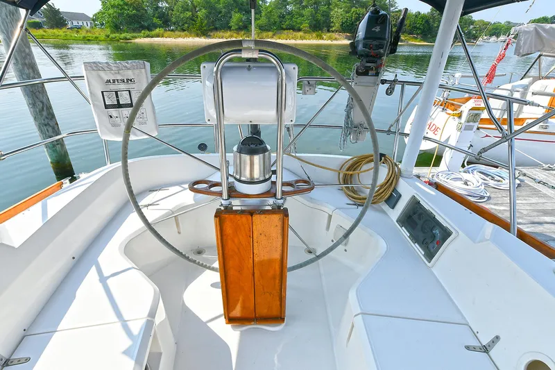 The Verdict III Yacht Photos Pics 2002 Sabre 452 sailboat helm with wooden wheel, docked by a serene waterfront.
