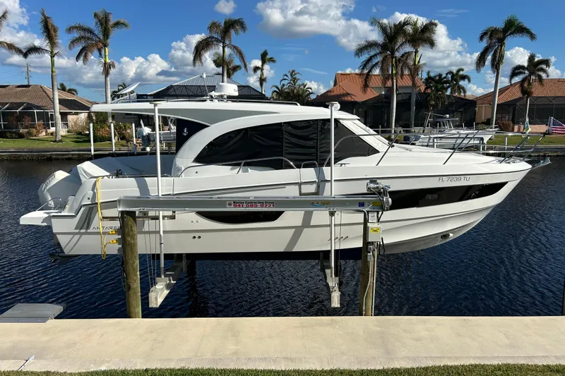  Yacht Photos Pics 2024 Beneteau Antares 11 boat docked by waterfront homes, under a clear blue sky.