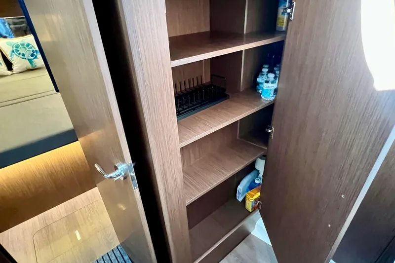  Yacht Photos Pics 2024 Beneteau Antares 11 interior storage cabinet with shelves and bottled water.