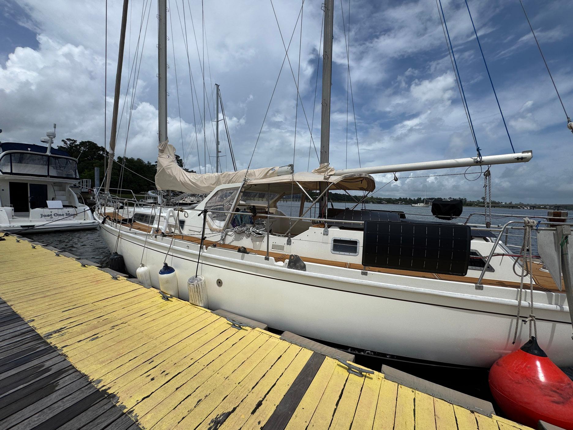 Sailboat Amel Mango 52, 1980 model, docked at marina with cloudy sky background.