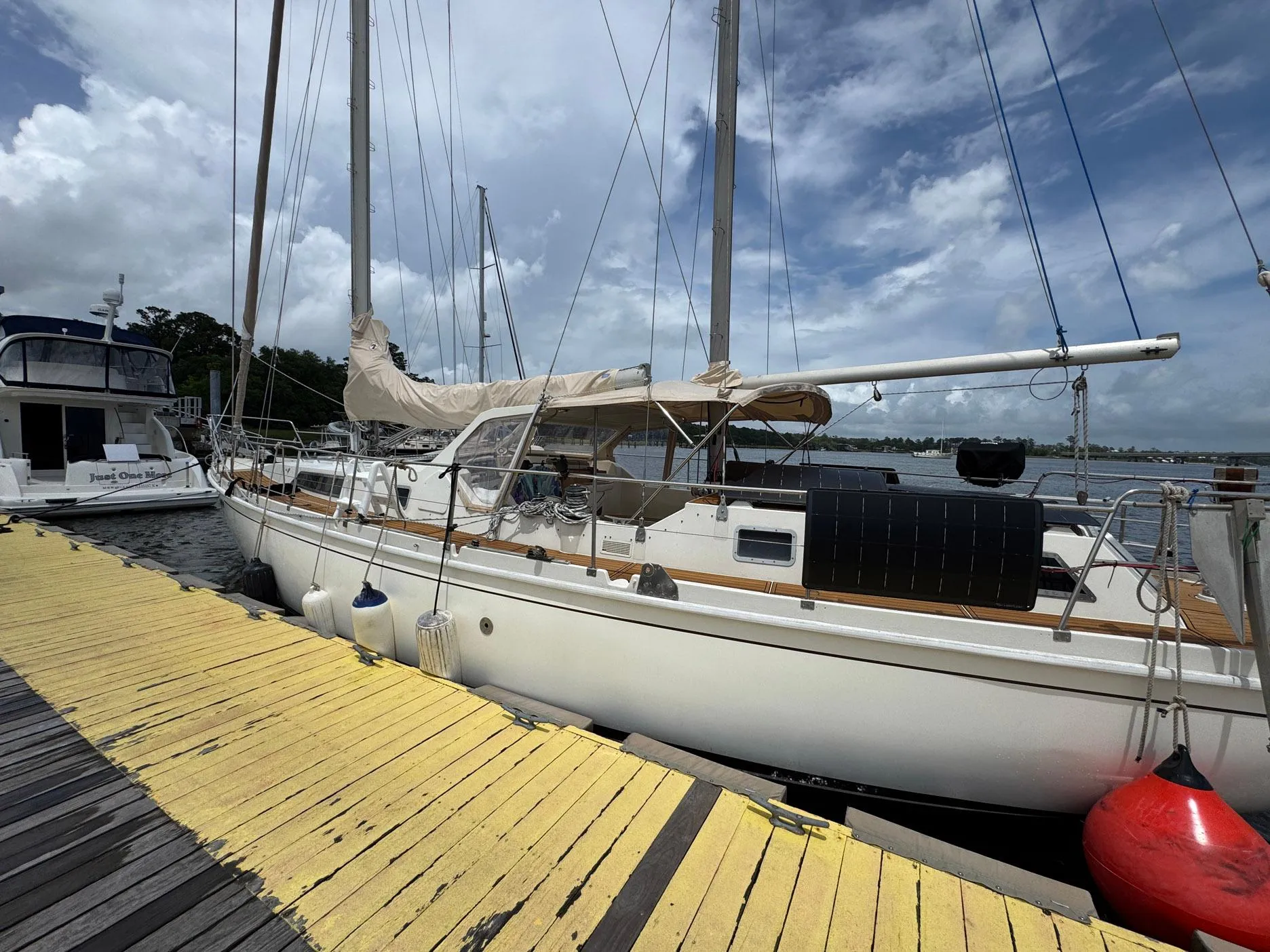 Sailboat Amel Mango 52, 1980 model, docked at marina with cloudy sky background.