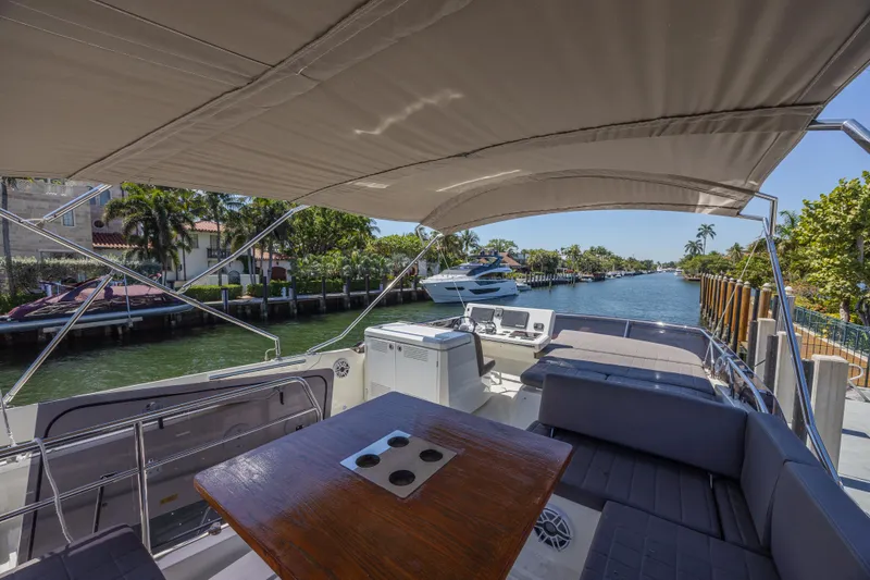 Aura Yacht Photos Pics Flybridge view of 2018 Prestige 520 yacht, featuring seating and table, docked by a scenic canal.