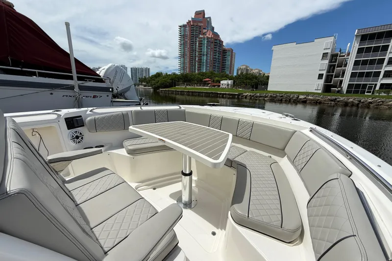  Yacht Photos Pics 2022 Pursuit S 358 Sport boat with luxurious seating and table, docked near modern buildings.