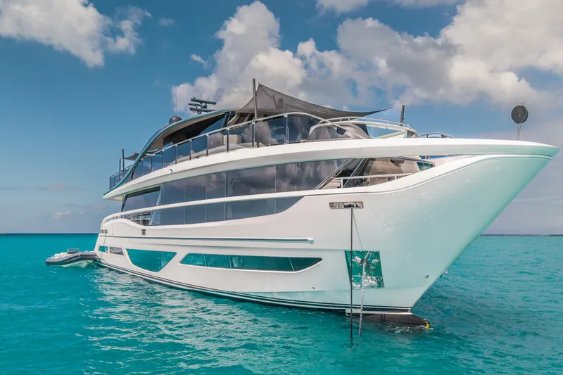 Gemini Yacht Photos Pics Luxurious 2023 Princess X95 yacht on turquoise waters under a partly cloudy sky.