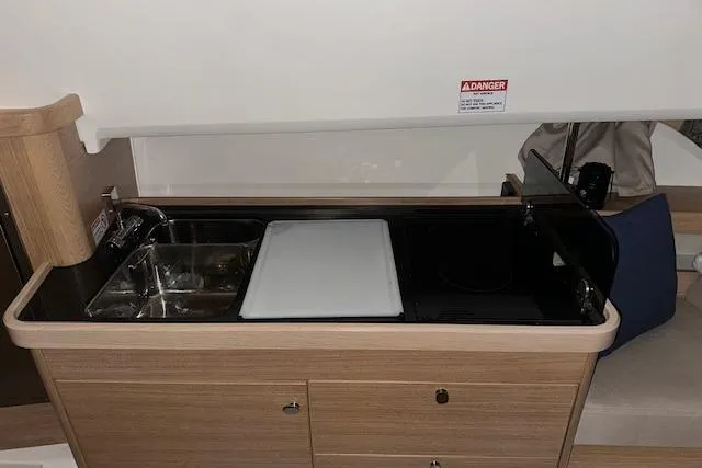  Yacht Photos Pics 2023 Nimbus C11 kitchenette with sink, cutting board, and stove in compact wooden design.