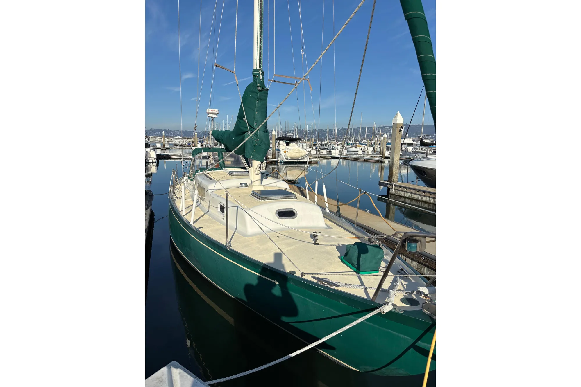 1968 Spencer 35 sailboat docked in a marina, featuring green accents and clear blue skies.