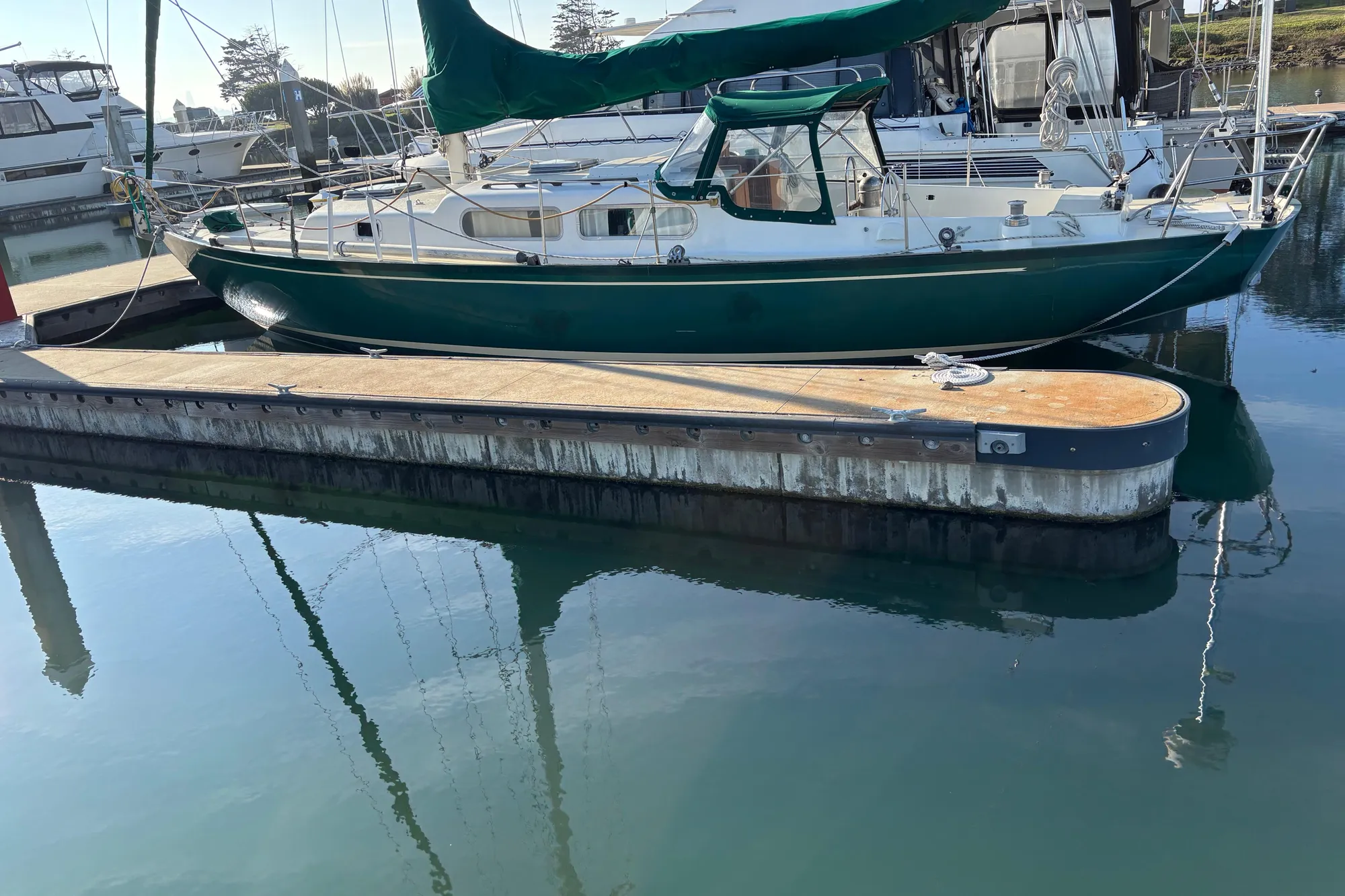 Sailboat docked at marina, Spencer 35 model, 1968, with green canopy and calm water reflection.
