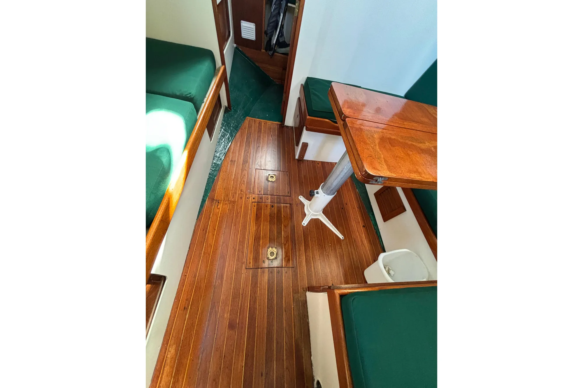 Interior of 1968 Spencer 35 sailboat with wooden flooring and green cushioned seating.