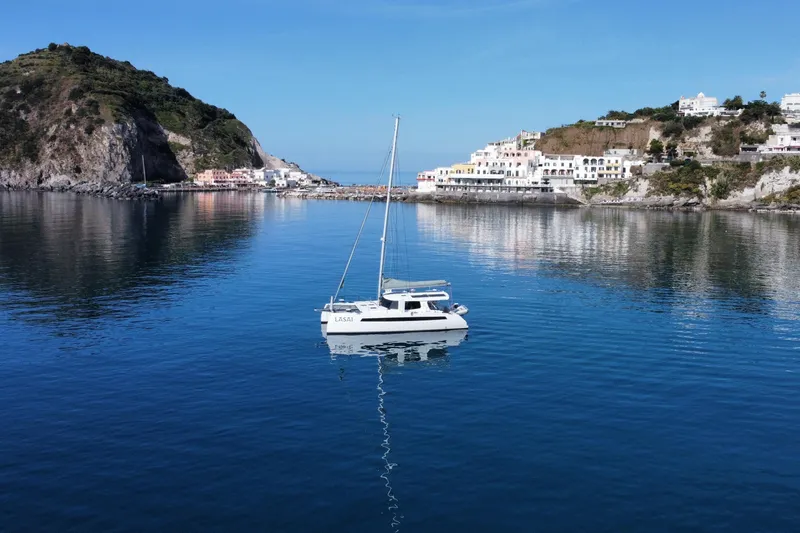 Lasai Yacht Photos Pics Sailboat "Balance 442" in serene coastal waters, surrounded by scenic cliffs and buildings, 2023.