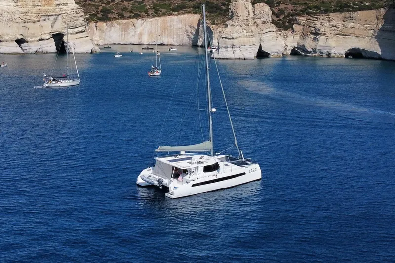 Lasai Yacht Photos Pics A 2023 Balance 442 catamaran sailing in a serene blue bay with rocky cliffs.