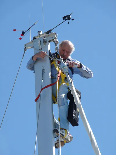 Alcyone Yacht Photos Pics Man working on Catalina 350 sailboat mast, clear blue sky background.